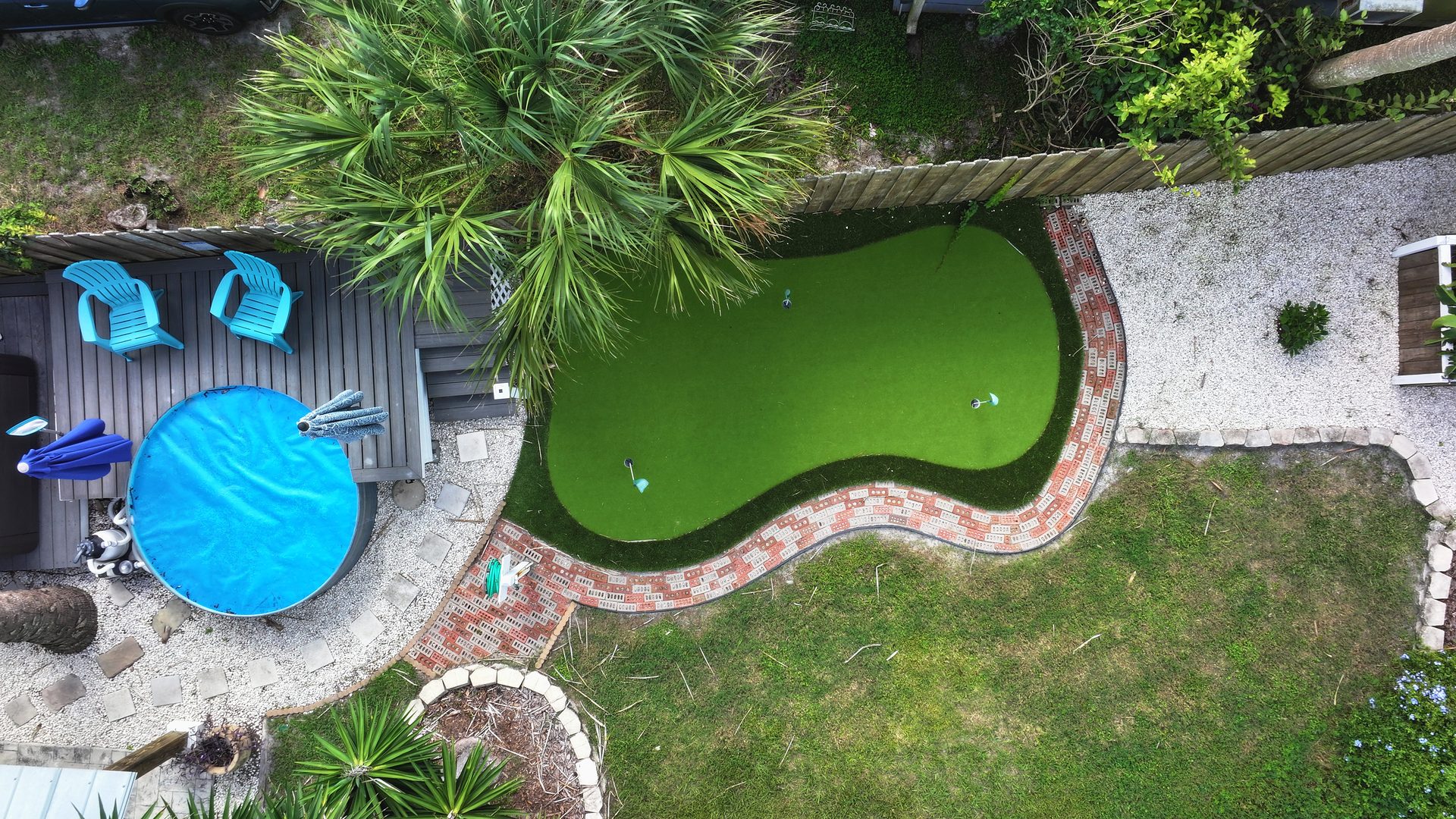 Cleaned drone aerial over a backyard with a covered plunge pool, deck seating, and a putting green