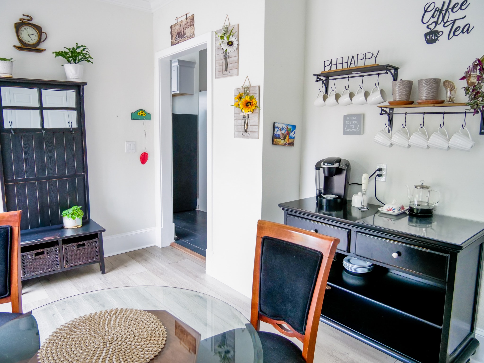 Kitchen and dining area with a coffee bar, hanging mugs, a glass dining table, and a dark wood hall tree