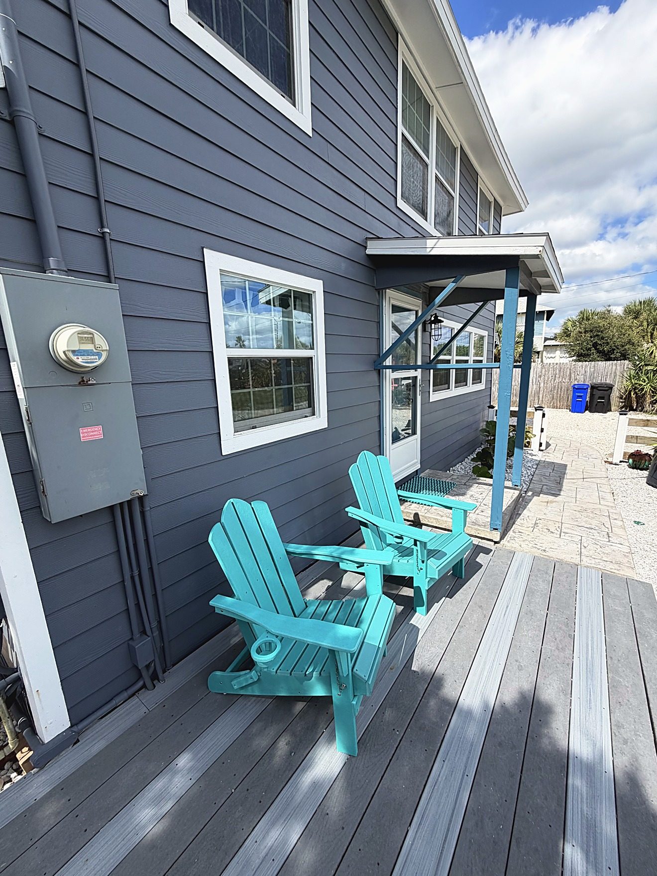 Front deck of a coastal home with two turquoise Adirondack chairs against blue-gray siding