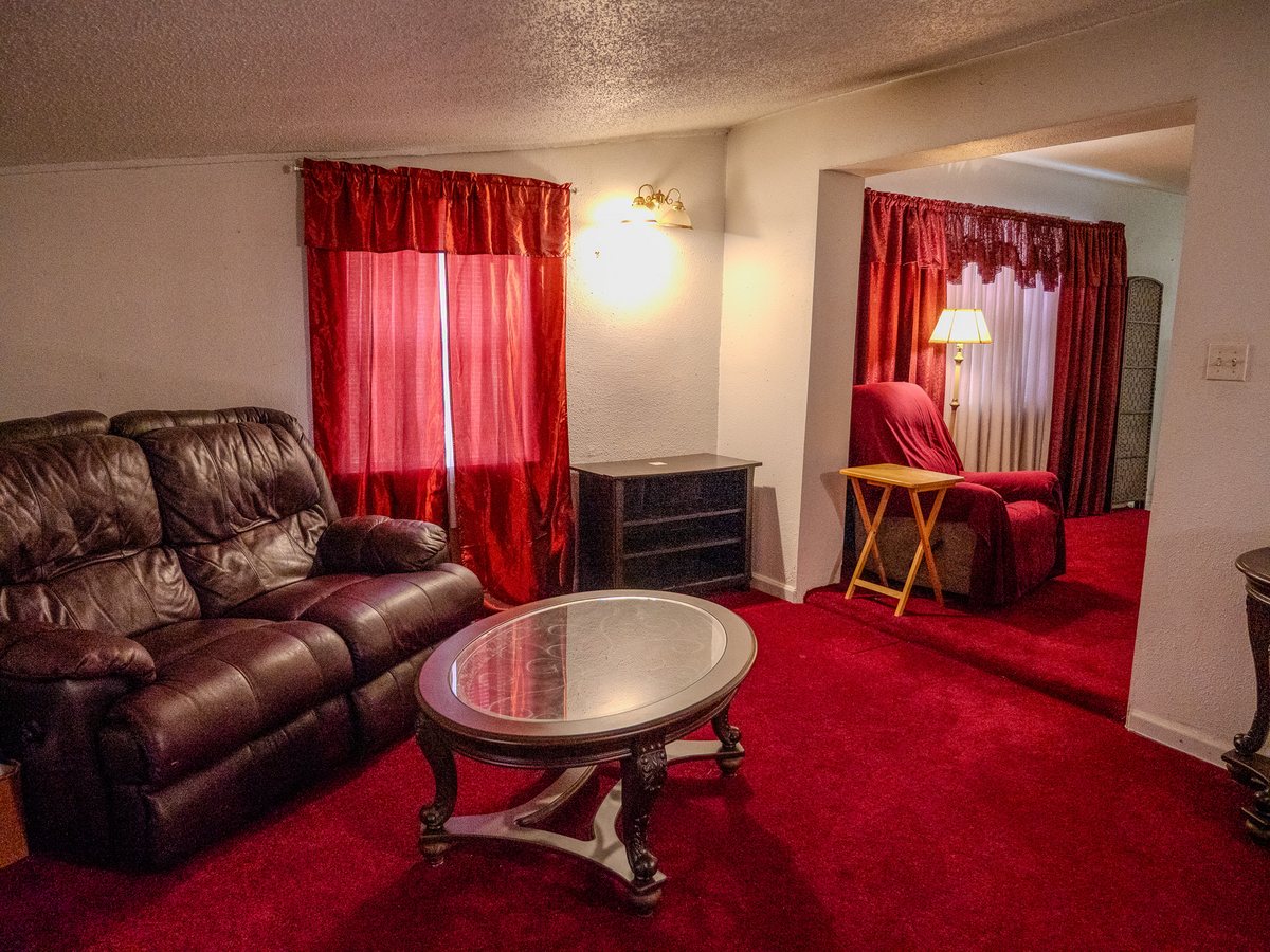 Living room with a brown leather loveseat, glass-top coffee table, and red carpet and curtains in a Jacksonville home