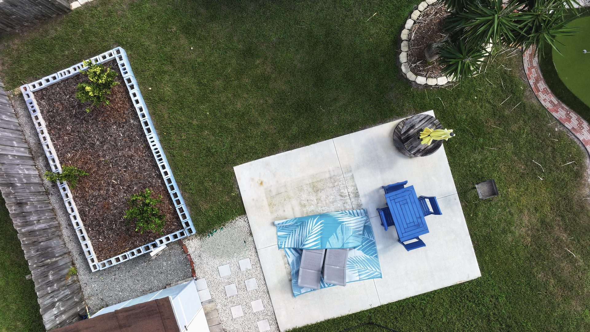 Cleaned drone aerial looking straight down on a backyard patio, garden bed, and lawn