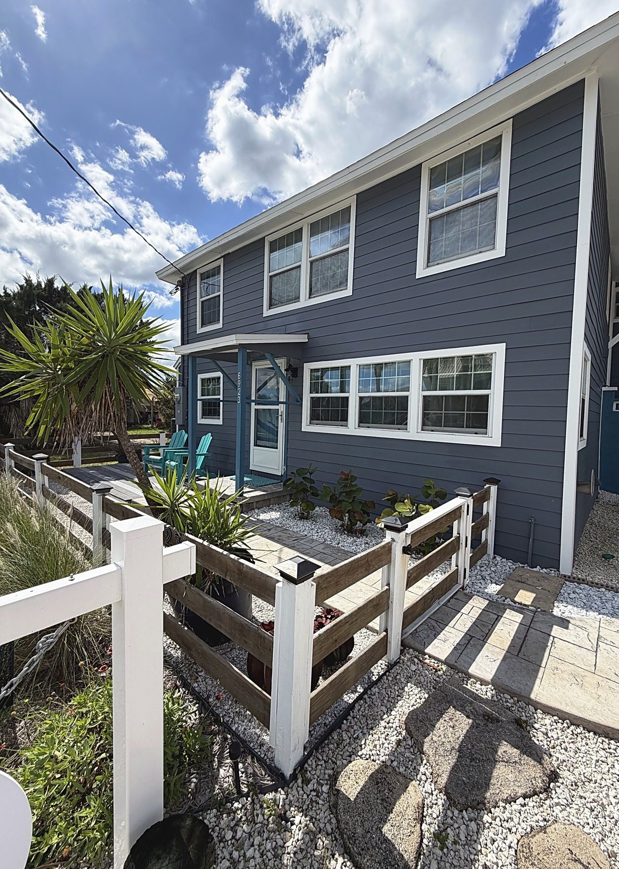 Angled front exterior of a two-story coastal home with a fenced front deck and gravel walkway