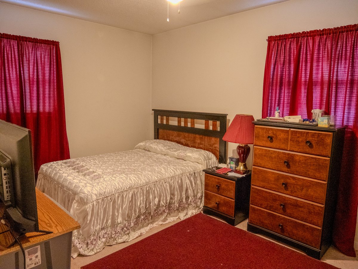 Bedroom with a made bed, wood nightstand and dresser, and red curtains in a Jacksonville home