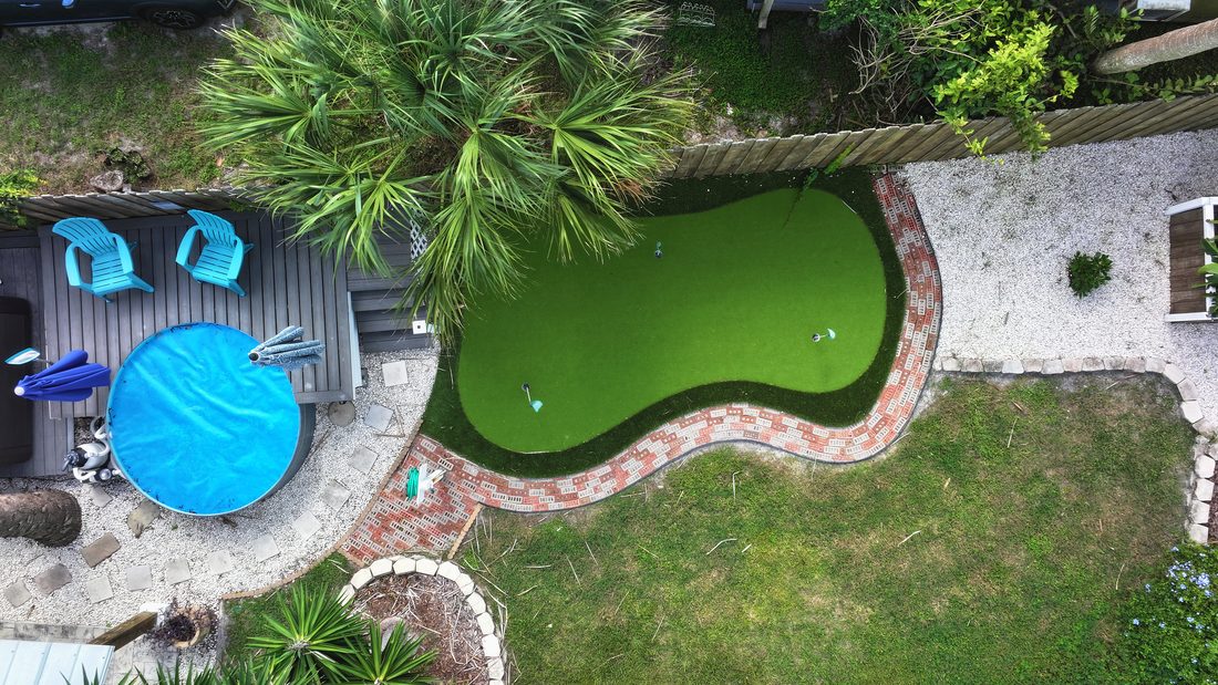 Aerial view of a backyard with a covered pool, deck, and putting green