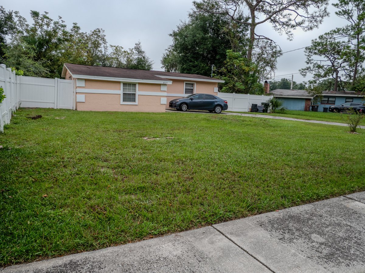 Front exterior of a peach single-story home with a white vinyl fence and a wide front lawn in Jacksonville, Florida