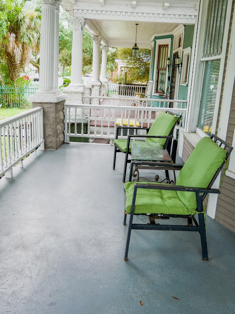 Wraparound porch with green cushioned chairs and white columns